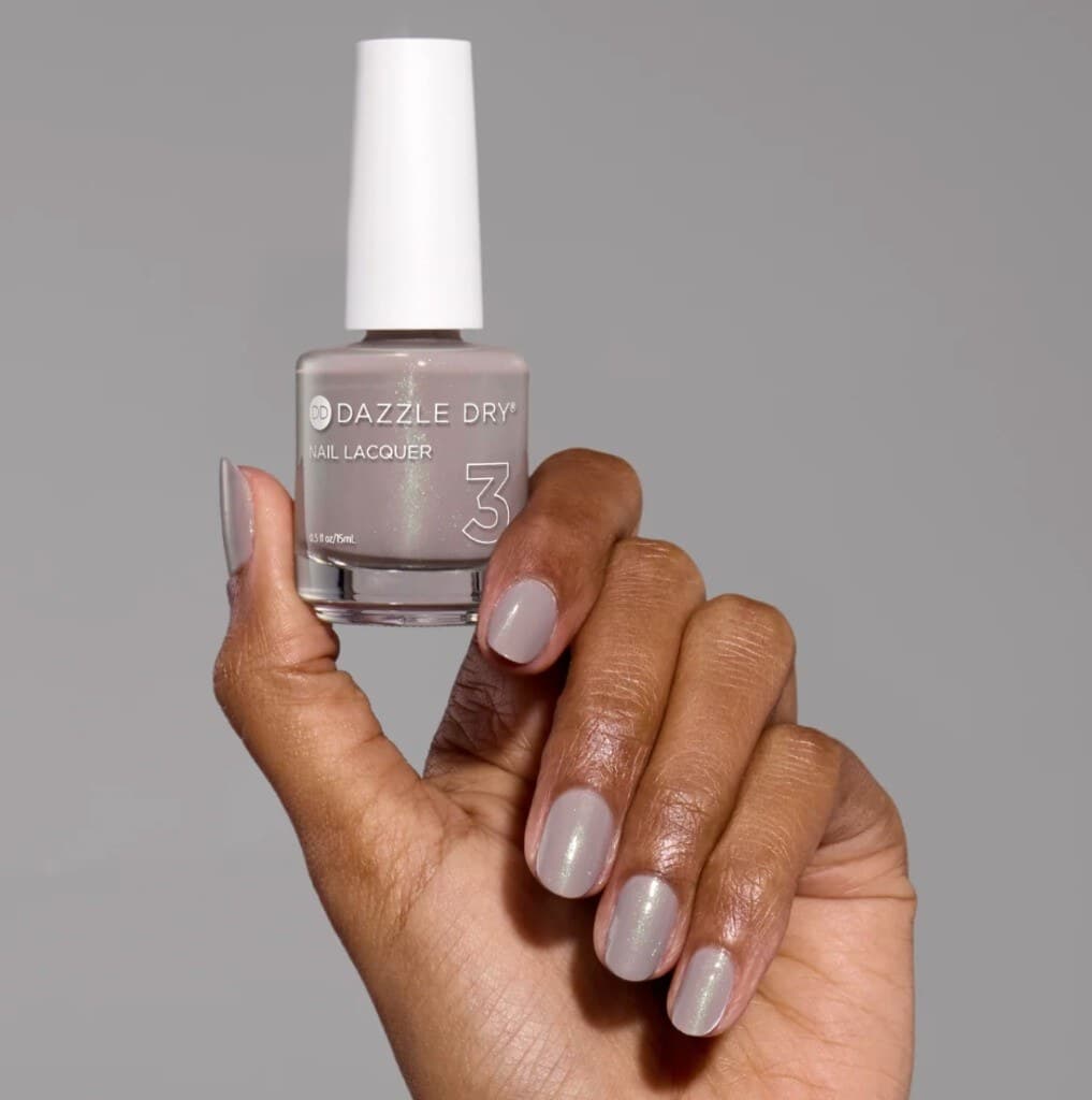 Hand with a Dazzle Dry nail lacquer bottle and matching manicure