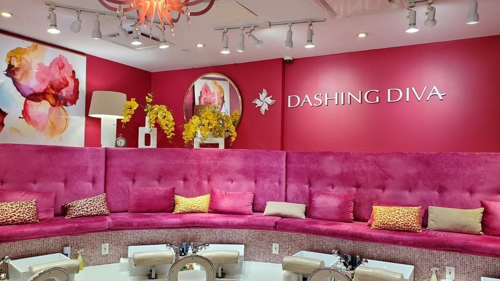 Dashing Diva pedicure lounge — pink tufted seating with cushions under the branded wall sign